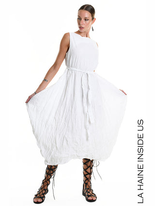 La Haine Dress 5378 white: Modisches, ärmelloses Kleid mit geknitterter Baumwollstruktur, ballonartigem Rock und Bindeschärpe, kombiniert mit schwarzen, knöchelhohen Gladiatorsandalen.