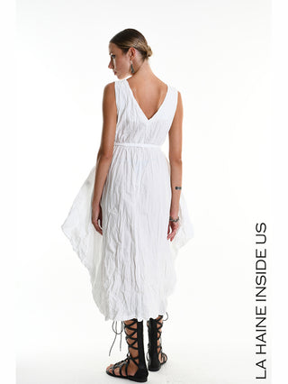 La Haine Dress 5378 white, ein ärmelloses, knitteroptik Kleid mit V-Ausschnitt und Taillenband, kombiniert mit schwarzen Gladiator-Sandalen und langen Ohrringen, präsentiert von einer Frau mit Dutt.