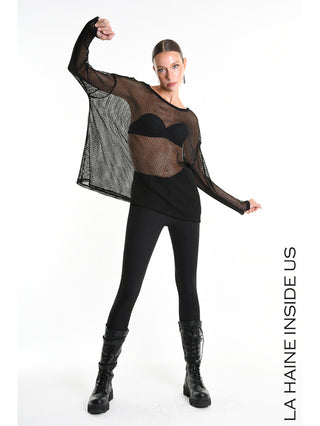 La Haine Sweater 5344 black: Model trägt lockeren, grobmaschigen schwarzen Netzpullover mit Rundhalsausschnitt, langen Ärmeln und Seitenschlitz. Kombiniert mit schwarzem Bralette, Leggings und klobigen Schnürstiefeln.