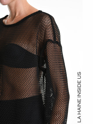 Person trägt La Haine Sweater 5344 black in grobmaschigem Netzstoff, lockerem Schnitt. Sichtbare Schultern und Schlüsselbein durch transparentes Gewebe; seitlicher Schlitz betont moderne Ästhetik.
