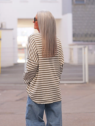 Eine Person trägt das OFF#DLY Longsleeve Lousiana khaki/white mit olivgrünen und weißen Streifen, lockerer Schnitt, ideal für lässige Alltagslooks, kombiniert mit hellen Jeans.