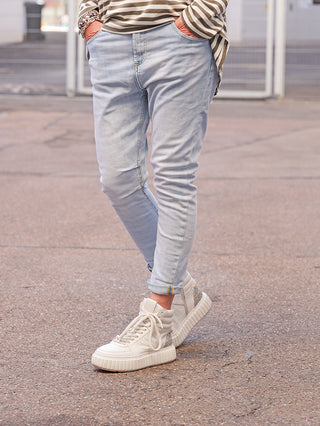 Person trägt OFF#DLY Denim Padua blue, eine schlanke, hell gewaschene Jeans, leicht hochgekrempelt, kombiniert mit weißen Sneakers und einem gestreiften Shirt.