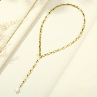 OFF#DLY Y Kette m. Perle KTD707 gold: Eine filigrane Y-förmige Halskette aus goldenen Papierclip-Gliedern mit einem weißen Perlenanhänger, präsentiert auf einem cremefarbenen Hintergrund, dekoriert mit trockenen Gräsern.
