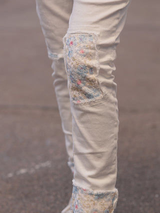 Nahaufnahme der OFF#DLY Denim White Flowers zeigt beigen Jeansstoff mit floralen Patches an Knie und Saum, die dem Design eine feminine Note verleihen. Ideal für vielseitige Stylings.