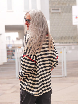 Person trägt das OFF#DLY Ringel Shirt Ulla black/red mit schwarz-weißen Streifen und rotem Rand, locker fallend im urbanen Umfeld. Perfekt für lässige, stilvolle Alltagsoutfits.