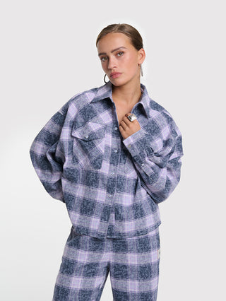 Frau trägt ALIX Checked Blouse night blue, eine locker geschnittene, karierte Flanellbluse mit Knopfleiste. Die Bluse hat einen leicht verkürzten Schnitt und Strass-Schriftzug auf der Rückseite.