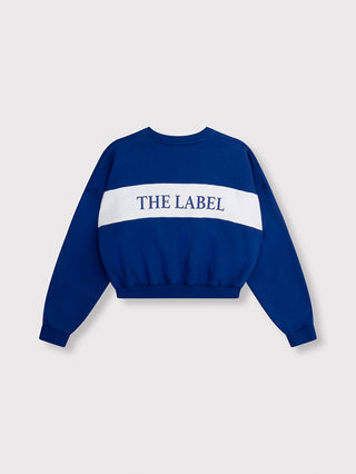 ALIX Logo Tape Sweater royal blue zeigt ein verkürztes, langärmeliges Sweatshirt mit einem breiten weißen Band THE LABEL auf dem Rücken, gerippten Bündchen und sportlicher Silhouette.