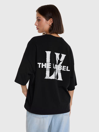 ALIX Faded LX Shirt black zeigt einen markanten weißen Rückenprint mit THE LABEL und überlappenden Buchstaben. Lockerer Schnitt, kombiniert mit Jeans, betont den lässigen Streetstyle.