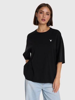 Junge Frau trägt das ALIX Faded LX Shirt black, ein oversized schwarzes T-Shirt mit weißem Bull-Logo auf der Brust, kombiniert mit hellblauen Jeans und langen, dünnen Creolen.