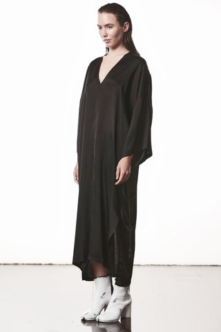 Thom Krom Dress WD 61 black: Modell trägt ein oversized, langes schwarzes Kleid mit V-Ausschnitt und weiten Kimono-Ärmeln, kombiniert mit weißen, klobigen Stiefeln und Präsentation eines minimalistischen, avantgardistischen Looks.