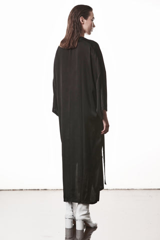 Person von hinten in Thom Krom Dress WD 61 black, einem oversized, fließenden Sateen-Kleid mit tiefem V-Ausschnitt und langen seitlichen Schlitzen, getragen über weißen, chunky-heeled Boots.