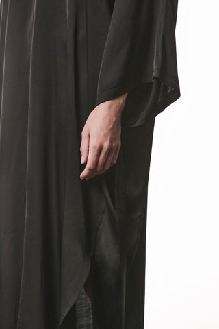 Nahaufnahme einer Hand, die den fließenden Stoff des Thom Krom Dress WD 61 black berührt, zeigt die lockere Passform und den eleganten Fall des glänzenden, schwarzen Sateen-Kleides.