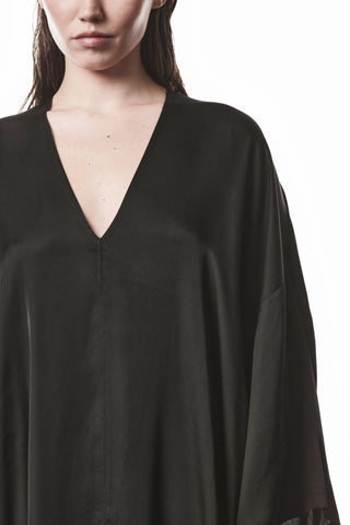 Person trägt Thom Krom Dress WD 61 black, ein oversized schwarzes Kleid mit tiefem V-Ausschnitt. Der fließende Sateen-Stoff erzeugt eine elegante Bewegung und unterstreicht den avantgardistischen Look.