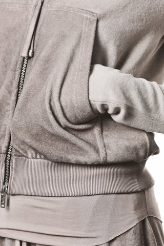 Nahaufnahme der Thom Krom Jacke WSJ 496 stone, die einen Reißverschluss, eine Kängurutasche und gerippte Bündchen zeigt. Die Hand des Trägers steckt in der Tasche.