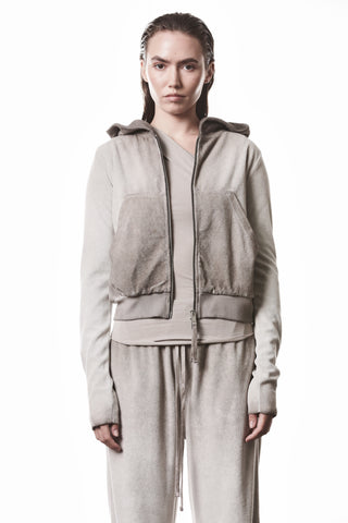 Junge Frau in einem Thom Krom Jacke WSJ 496 stone, figurbetontem Schnitt mit Kapuze und Reißverschluss, zeigt sportlich-minimalistische Avantgarde-Ästhetik in hochwertiger Terry-Qualität und markanter Logo-Stickerei.