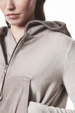 Nahaufnahme einer Person mit Thom Krom Jacke WSJ 496 stone, leicht geöffneter grauer Kapuzenpullover mit Metallreißverschluss und flach liegender Kapuze, betont modernes avantgardistisches Design.