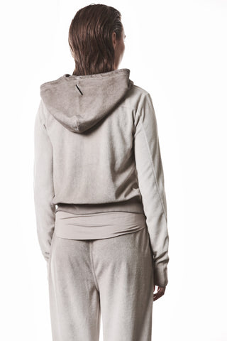 Rückansicht einer Person in einem Thom Krom Jacke WSJ 496 stone Tracksuit aus Velours, bestehend aus einer Kapuzenjacke mit Reißverschluss und passenden Hosen, minimalistisch und sportlich gestaltet.