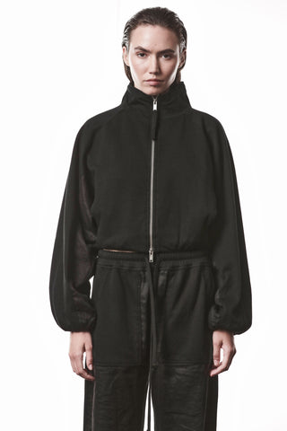 Thom Krom Jacke WSJ 497 black, hochgeschlossener Sweatshirt mit Reißverschluss, leicht oversized, strukturierter Stoff, Daumenöffnungen, getragen zu locker sitzenden, schwarzen Hosen mit Kordelzug und sichtbaren Taschen.