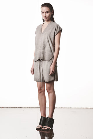 Junge Frau trägt das Thom Krom Tee WTS 610 stone, ein locker geschnittenes, ärmelloses V-Neck-Top, kombiniert mit passendem Rock und minimalistischen schwarzen Sandalen.