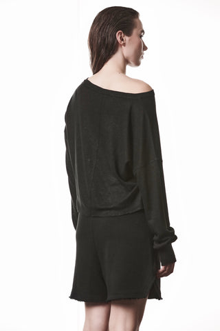 Eine Person trägt das Thom Krom Tee WTS 613 black mit einem Bootsausschnitt, der eine Schulter freilegt, kombiniert mit langen Ärmeln und Daumenöffnungen, zusammen mit schwarzen Shorts.