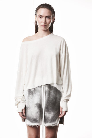 Junge Frau trägt das Thom Krom Tee WTS 613 offwhite, ein lässig geschnittenes, off-shoulder Langarmshirt mit Bootsausschnitt und Daumenöffnungen, kombiniert mit grauen, fransigen Shorts.