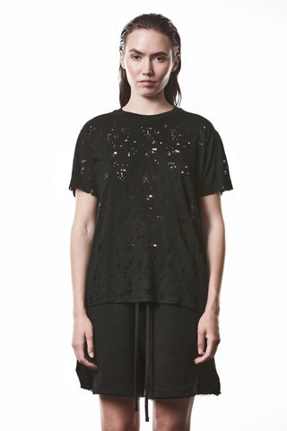 Eine Frau trägt das Thom Krom Tee WTS 620 black, ein schwarzes T-Shirt mit Rundhalsausschnitt, markantem Allover-Destroy-Effekt und raw cut Abschlüssen, kombiniert mit einem schwarzen Drawstring-Rock.