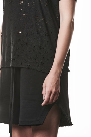 Nahaufnahme einer Person mit dem Thom Krom Tee WTS 620 black. Das Shirt zeigt einen markanten Allover-Destroy-Effekt mit Raw Cut Abschlüssen, kombiniert mit einem schwarzen Rock oder Shorts mit sichtbarem Kordelzug.