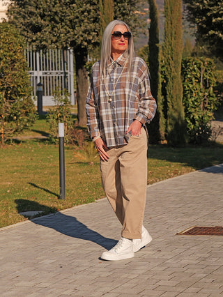 Ältere Frau trägt die Oversize OFF#DLY Bluse Susi blue/brown mit Karomuster, lockerer Passform, über beige Hosen. Die Bluse fällt lässig und bietet Bewegungsfreiheit.