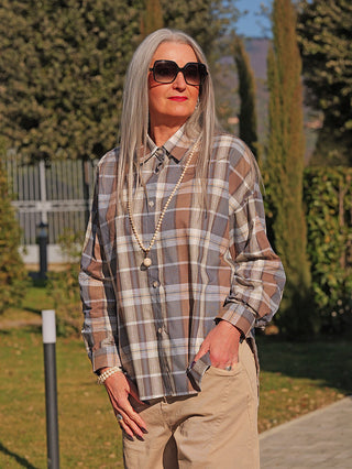 Die OFF#DLY Bluse Susi blue/brown zeigt eine Frau im Garten, mit grauem Haar und Sonnenbrille, in einer locker fallenden, übergroßen Karo-Bluse aus Baumwolle und Leinen, kombiniert zu hellen Hosen.