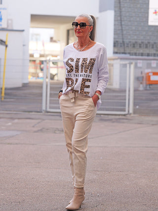 Frau trägt OFF#DLY Joggpant Luise sand, eine bequeme beige Hose mit hohem Bund und Bindegürtel, kombiniert mit heeled Boots. Sie strahlt lässige Eleganz aus.