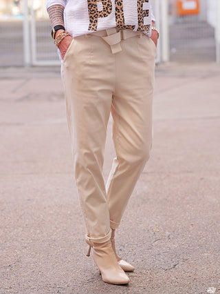 Nahaufnahme einer Person, die die OFF#DLY Joggpant Luise sand trägt. Die Hose ist beige, mit integriertem Stoffgürtel, zeigt eine schmale Silhouette und ist in die Taschen gesteckt.