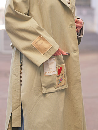 OFF#DLY Mantel Jessy Verde mit stilvollen Patches, darunter ein PARIS-Patch und ein rotes Herz. Der Ärmel zeigt ein EXPLORE INFINITY-Label. Hand teils in der Tasche.