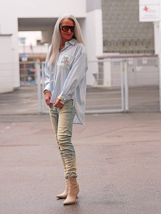 Ältere Person im urbanen Umfeld trägt die OFF#DLY Bluse Ancona stripes lightblue. Die Streifenbluse besticht durch Oversize-Schnitt, Brusttasche mit Print und passt perfekt zu den dezenten Jeans und Stiefeletten.