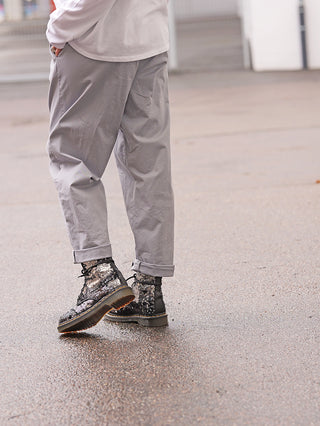 Person in OFF#DLY Denim Jogger Lightgrey, leicht konisch geschnitten und an den Knöcheln leicht hochgekrempelt, steht auf nassem Boden. Hände in den Taschen, Hintergrund unscharf urban.