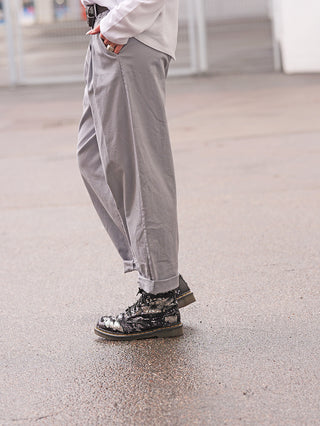 Person trägt OFF#DLY Denim Jogger Lightgrey mit lockerem, komfortablem Schnitt und Stretch. Hose ist an den Knöcheln gekrempelt, kombiniert mit schwarzen, glänzenden Stiefeletten.