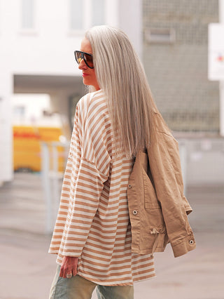 Eine Person trägt das OFF#DLY Longsleeve Lousiana beige/white mit beigen und weißen Streifen, ergänzt durch lässigen, lockeren Schnitt und 3-D-Print. Eine beige Jacke ist lässig über die Schulter drapiert.