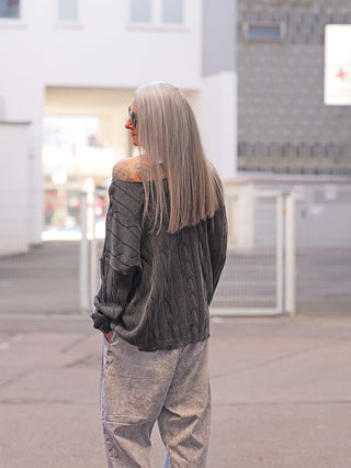 Person von hinten, trägt den OFF#DLY Pulli Agathe black mit lockerem Schnitt. Der Pullover fällt off-the-shoulder, zeigt ein feines Strukturmuster, kombiniert mit hellen, weit geschnittenen Hosen.