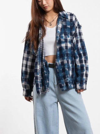 Frau trägt OUTRYGHT Milo blue combo, eine locker sitzende, blau-weiße karierte Baumwollbluse im leicht verwaschenen Look, über einem weißen Crop-Top, passend zu hellen, weiten Jeans.