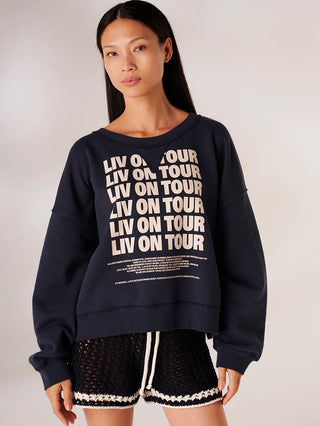 Modell trägt LIV Bergen Graz Tour neon green Sweatshirt mit LIV ON TOUR Print, kombiniert mit schwarzen Shorts. Sweatshirt ist leicht oversized und vermittelt einen urbanen, lässigen Stil.
