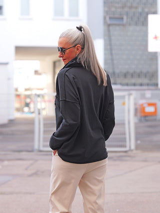 Person trägt den OFF#DLY LS Thea black Hoodie mit hohem Zopf, dunkler Sonnenbrille. Der Hoodie zeichnet sich durch ein auffälliges Herz-Design auf der Vorderseite aus.