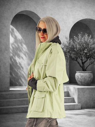 Person im Profil mit silbrig-grauem Haar trägt die OFF#DLY Parka Como verde, eine lässig-elegante, feldgrüne Jacke mit aufgesetzten Taschen, über einem dunklen Oberteil und Jeans.