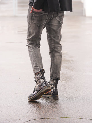 OFF#DLY Denim Siena black/grey, getragene graue Jeans mit Used-Waschung und Destroy-Details, kombiniert mit glänzenden, silbernen Paillettenstiefeln auf nassem Gehweg.