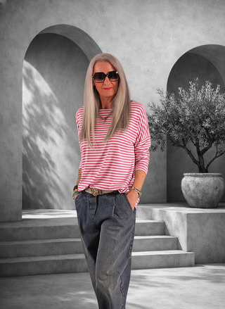 Frau trägt das OFF#DLY Ringelshirt Frida pink/white mit horizontalen Streifen und lockerem Schnitt, kombiniert mit dunklen Jeans in minimalistischer Umgebung.