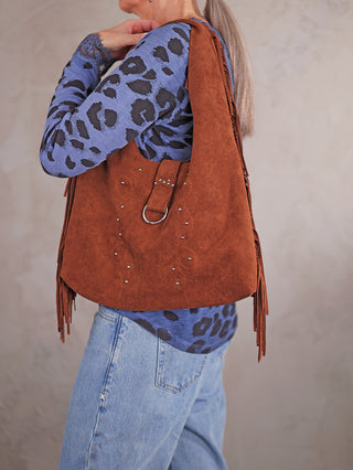 Die OFF#DLY Fransen Bag coffee zeigt braunes Wildlederimitat mit Fransen, Studs und Metallring. Tasche wird von Person mit blauem Leopardenmuster-Top und Jeans getragen. Maße: 36x30 cm.
