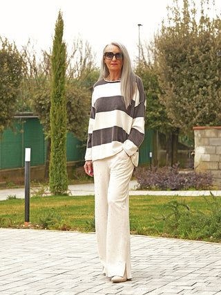 Frau trägt OFF#DLY Pulli Ancona black/creme, mit breiten Streifen und lockerem Schnitt, kombiniert mit weiten Hosen. Ideal für entspannten, stilvollen Alltagslook.
