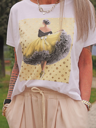 OFF#DLY Tee Ballerina white/gelb zeigt eine Illustration einer Frau in einem gelben, rüschigen Kleid. Kombiniert mit beigen Hosen und goldenen Accessoires, vermittelt es Eleganz und Stil.