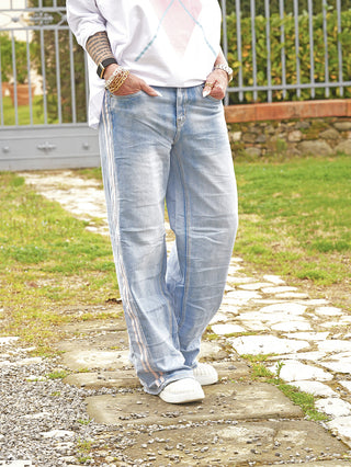 Person trägt OFF#DLY Denim Stripe blue/rose Jeans mit sportlichen Seitenstreifen; lockere Passform, Hände in Taschen, kombiniert mit weißen Slip-On-Sneakers und Armbändern, ideal für lässige Alltagslooks.