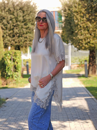 Ältere Frau in einem sonnenbeschienenen Gartenweg trägt das OFF#DLY Tee Shirt Vroni beige, ein locker sitzendes Oberteil mit feiner Spitze an Ärmeln und Saum, kombiniert mit lässigen Jeans.