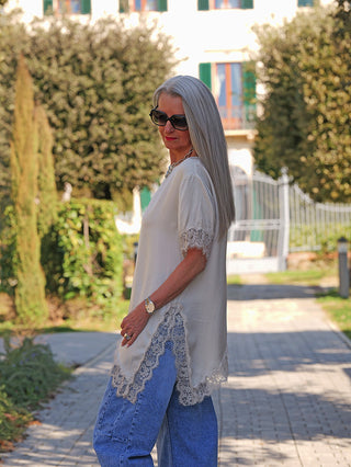 Frau trägt OFF#DLY Tee Shirt Vroni beige, ein locker geschnittenes, leicht fließendes Oberteil mit femininer Spitze an Ärmeln und Saum, kombiniert mit blauen Jeans und Accessoires.