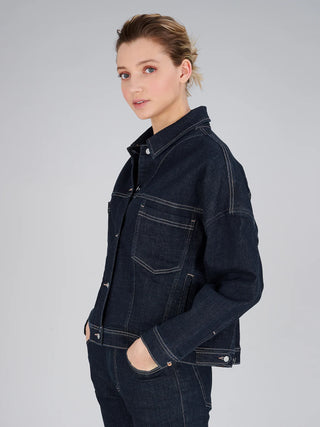 Frau trägt True Religion Amber Jacket Raw, eine lässige, oversize geschnittene Jeansjacke mit markanten Kontrastnähten und Brusttaschen, während sie in einer entspannten Pose vor neutralem Hintergrund steht.